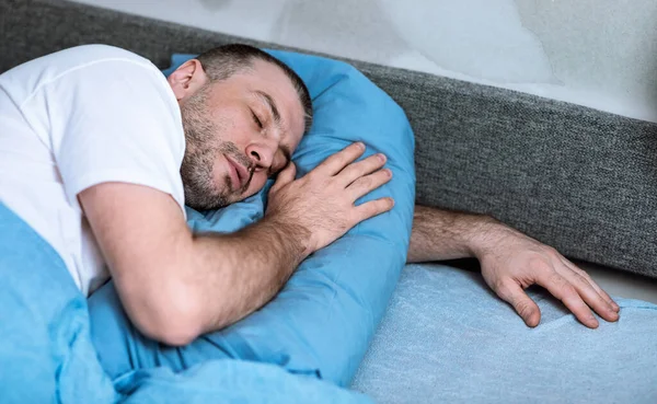 Чоловік спить обіймаючи подушку лежачи в ліжку залишаючись вдома — стокове фото