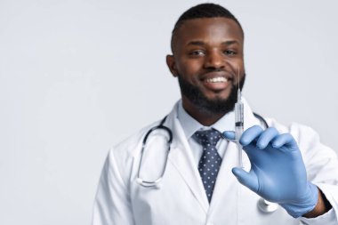Steteskopla gülümseyen siyah doktor elinde iğne tutuyor.