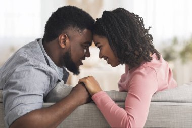 Romantik siyah çift evde kaynaşıyor, el ele tutuşuyor ve alınlarına dokunuyor.