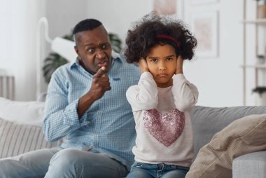 Kızgın Afrikalı Amerikalı büyükbaba torununa bağırıyor, kulaklarını kapatan çocuğa odaklanıyor.