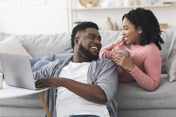 Lazer em casa. feliz casal afro-americano relaxante com laptop e café — Fotografia de Stock