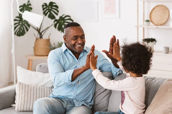 Quédate en casa, diviértete. Chica afroamericana pasando tiempo con el abuelo en el interior — Foto de Stock