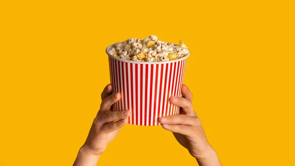 Oigenkännlig man som håller randig pappershink med popcorn på orange bakgrund, närbild. Panorama Ordförande — Stockfoto