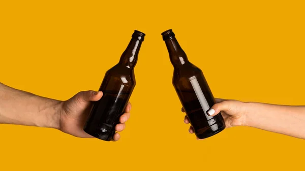 Erkek ve kadının elleri bira şişelerini tokuşturuyor, turuncu arka planda bir şeyi kutluyorlar, tasarım için maket yapıyorlar. — Stok fotoğraf