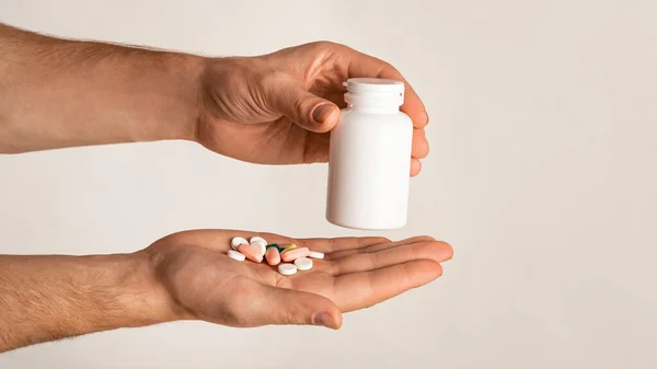 Unrecognizable guy holding bottle of meds and different pills on light background, space for design. Panorama — Stock Photo, Image