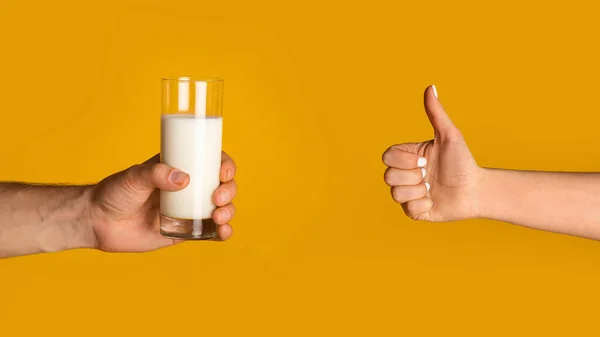 Manos de hombre joven sosteniendo vaso de leche y mujer mostrando los pulgares hacia arriba gesto sobre fondo naranja, espacio vacío —  Fotos de Stock