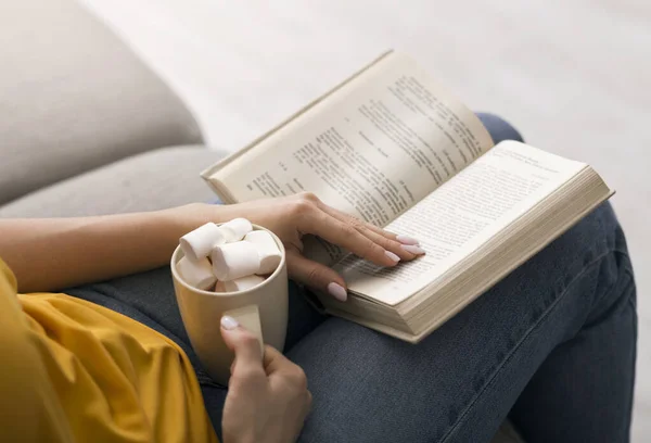 Resta a casa, leggi dei libri. Giovane ragazza godendo il suo drink con marshmallows e storia interessante sul divano, primo piano — Foto Stock