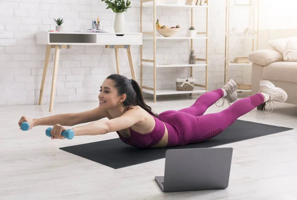 Active Hispanic woman watching online sports video and exercising with dumbbells at home