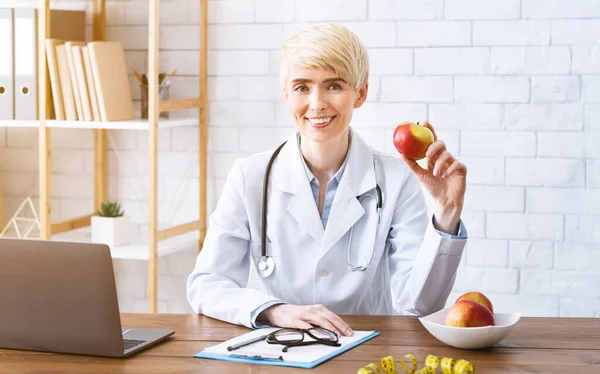 Доктор в офісі за столом з яблуком в руках — стокове фото