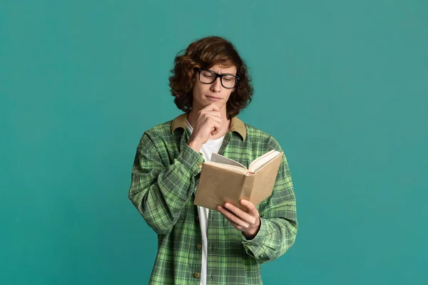 Okula dönelim. Gözlüklü çalışkan öğrenci turkuaz arka plan üzerine ilginç bir kitap okuyor. — Stok fotoğraf