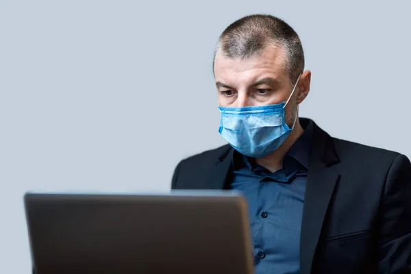 Бізнесмен працює на ноутбуці носіння медичної маски сидячи в студії — стокове фото