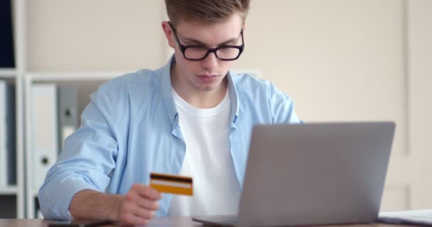 Jovem trabalhador fazendo transação financeira com cartão de crédito e laptop — Vídeo de Stock