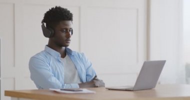 Kulaklıklı genç Afrikalı bir öğrenci dizüstü bilgisayarda Webinar izliyor.