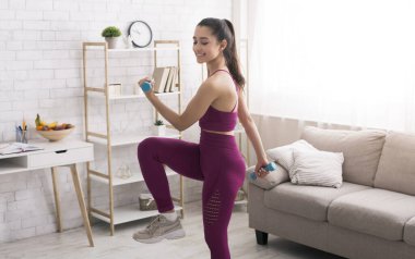 Evde kardiyo çalışmasında. Spor giyimli neşeli bir genç kız evde halterlerle egzersiz yapıyor.