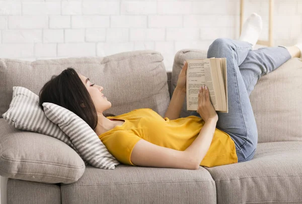 Карантинне дозвілля. Розумна жінка читає цікаву книгу на дивані вдома — стокове фото