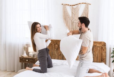 Güzel genç adam ve kadın yastıklarla savaşıyor.
