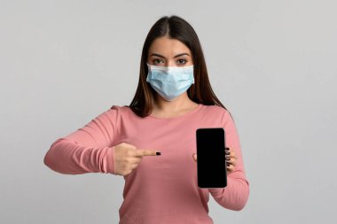 Tıbbi Maskeli Genç Kadın Siyah Ekranlı Akıllı Telefonu Gösteriyor