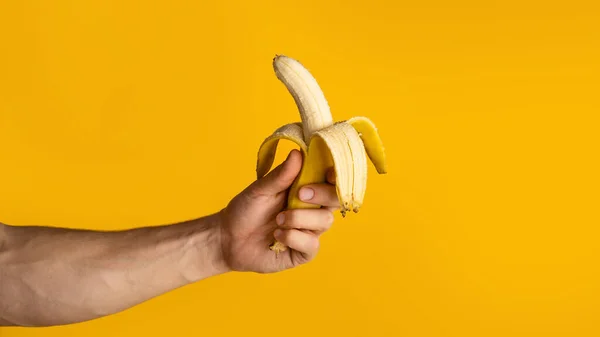 Primer plano del tipo sosteniendo plátano medio pelado sobre fondo naranja, espacio en blanco. Panorama —  Fotos de Stock