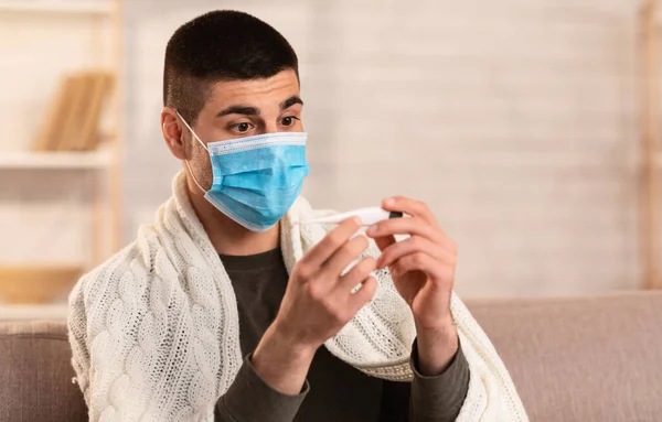Homem assustado com febre a olhar para o termómetro — Fotografia de Stock