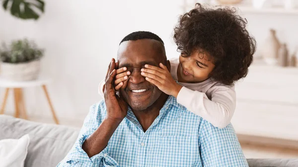 Gerações de ligação. Adorável menina afro-americana fechando os olhos de seus avós em casa, jogando jogo GUESS Quem — Fotografia de Stock