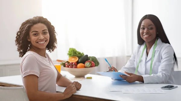 Dietólogo con historial médico y señora africana sonriendo a la cámara —  Fotos de Stock