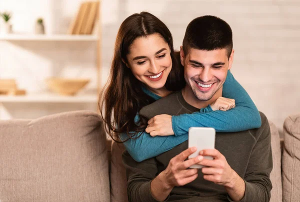 Casal encantador usando telefone celular sentado no sofá — Fotografia de Stock