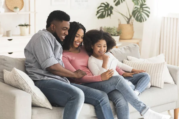 Padres negros felices y su hijita relajándose con smartphone en casa —  Fotos de Stock