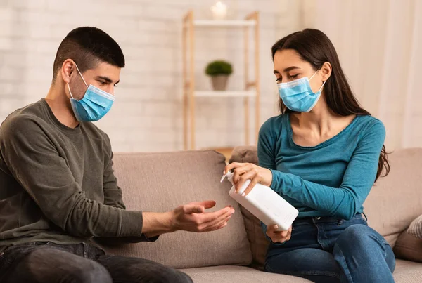 Pareja sentada en el sofá aplicando spray anti bacterias —  Fotos de Stock