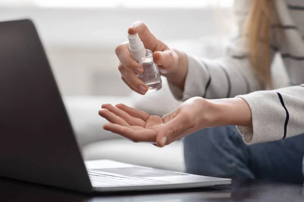 Woman pouring antibacterial gel on hands near laptop, close up