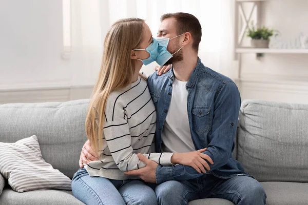 Молодая супружеская пара целуется в защитных медицинских масках — стоковое фото