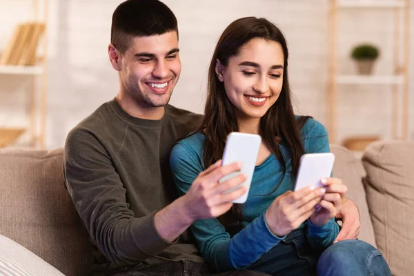 Pareja usando teléfonos celulares sentados en un sofá —  Fotos de Stock