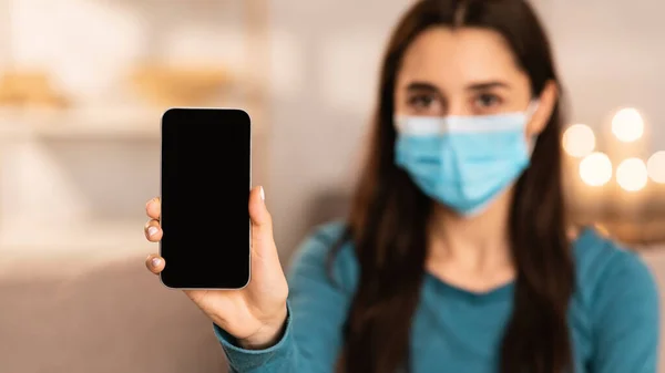 Женщина в хирургической маске показывает смартфон — стоковое фото