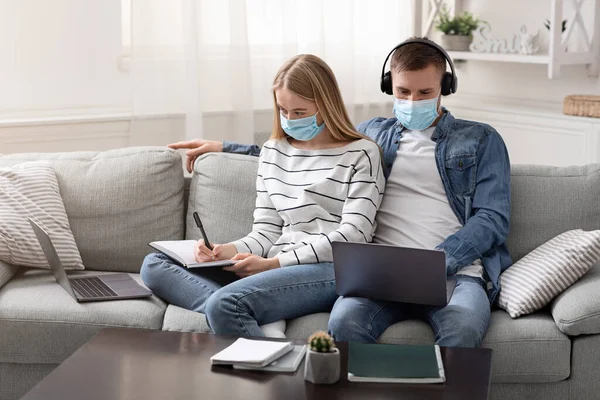 Young couple in protective masks working on laptops — Stock Photo, Image
