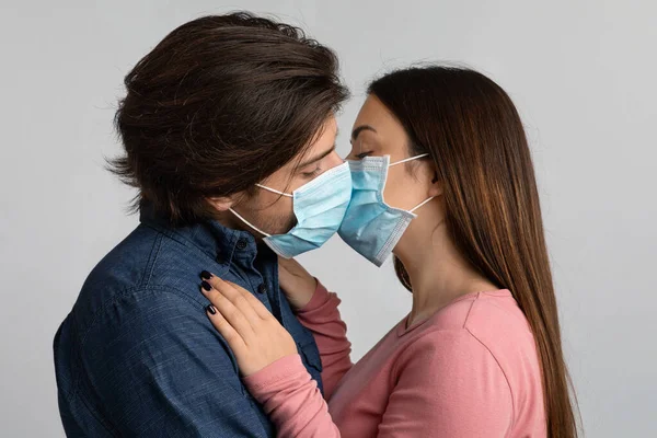 Millennial paar kussen elkaar tijdens het dragen van medische gezichtsmaskers — Stockfoto