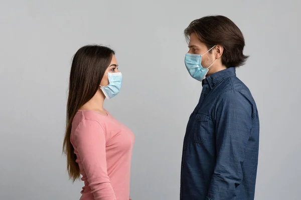 Κοινωνική απόσταση. Νεαρό ζευγάρι που φοράει ιατρικές μάσκες στέκεται πρόσωπο με πρόσωπο — Φωτογραφία Αρχείου