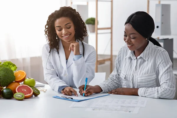 Senhora africana preencher formulário no consultório médico nutricionista — Fotografia de Stock