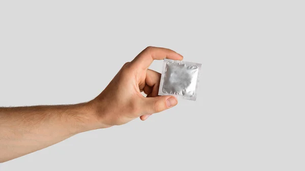 Concepto de sexo seguro. Joven con condón envuelto sobre fondo gris claro, espacio vacío. Panorama — Foto de Stock