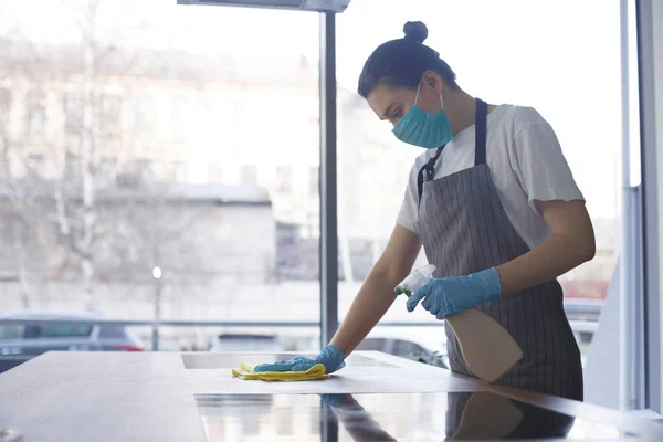 Giovane donna in maschera e guanti che fa la disinfezione della cucina — Foto Stock
