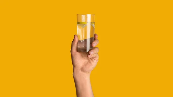 Joven mostrando un vaso de agua pura fresca sobre fondo naranja, cerca de la mano. Panorama — Foto de Stock