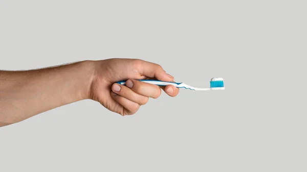 Oral hygiene. Young guy holding toothbrush with paste on light grey background, closeup. Panorama — Stock Photo, Image