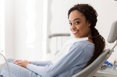 Gülümseyen Afrikalı kadın dişçi koltuğunda doktoru bekliyor.