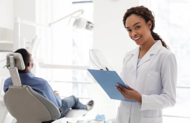 Gülümseyen kadın dişçi kabinede tıbbi form dolduruyor.