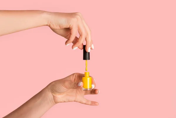 Jonge manicure openen nagellak fles op roze achtergrond, close-up. Lege ruimte — Stockfoto