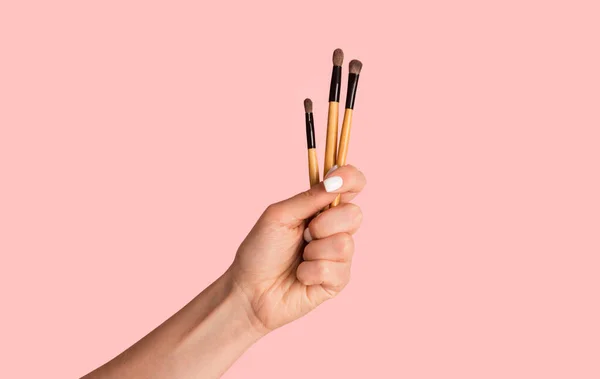 Closeup of beauticians hand showing lipstick or eyeshadow brushes on pink background — Stock Photo, Image