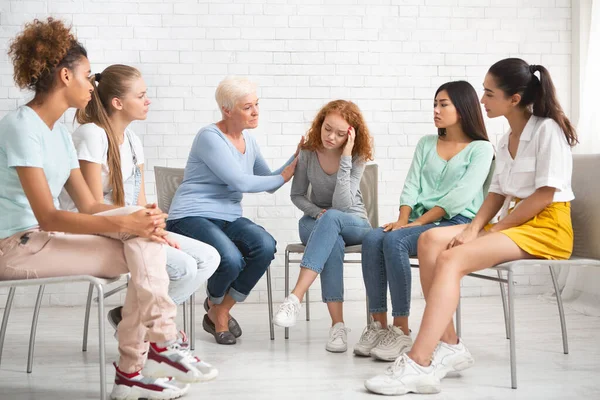 Psicólogo reconfortante chica durante la sesión de terapia con grupo de apoyo en interiores — Foto de Stock