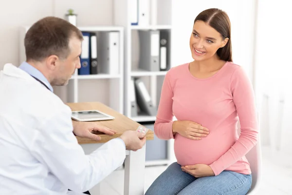 Mature experienced doctor showing pills to pregnant patient — Stock Photo, Image