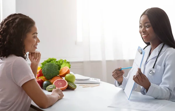 Mulher negra nutricionista mostrando prontuário do paciente feminino — Fotografia de Stock