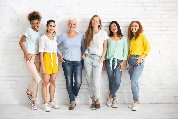 Diverse dames van verschillende leeftijd staande over witte bakstenen muur — Stockfoto