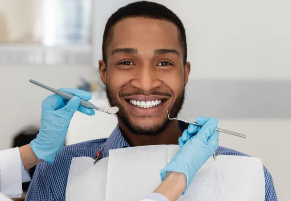 Молодий чорний чоловік у стоматологічному кріслі посміхається на камеру — стокове фото