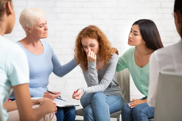 Зрелая леди утешает плачущую молодую женщину во время групповой психотерапии в помещении — стоковое фото
